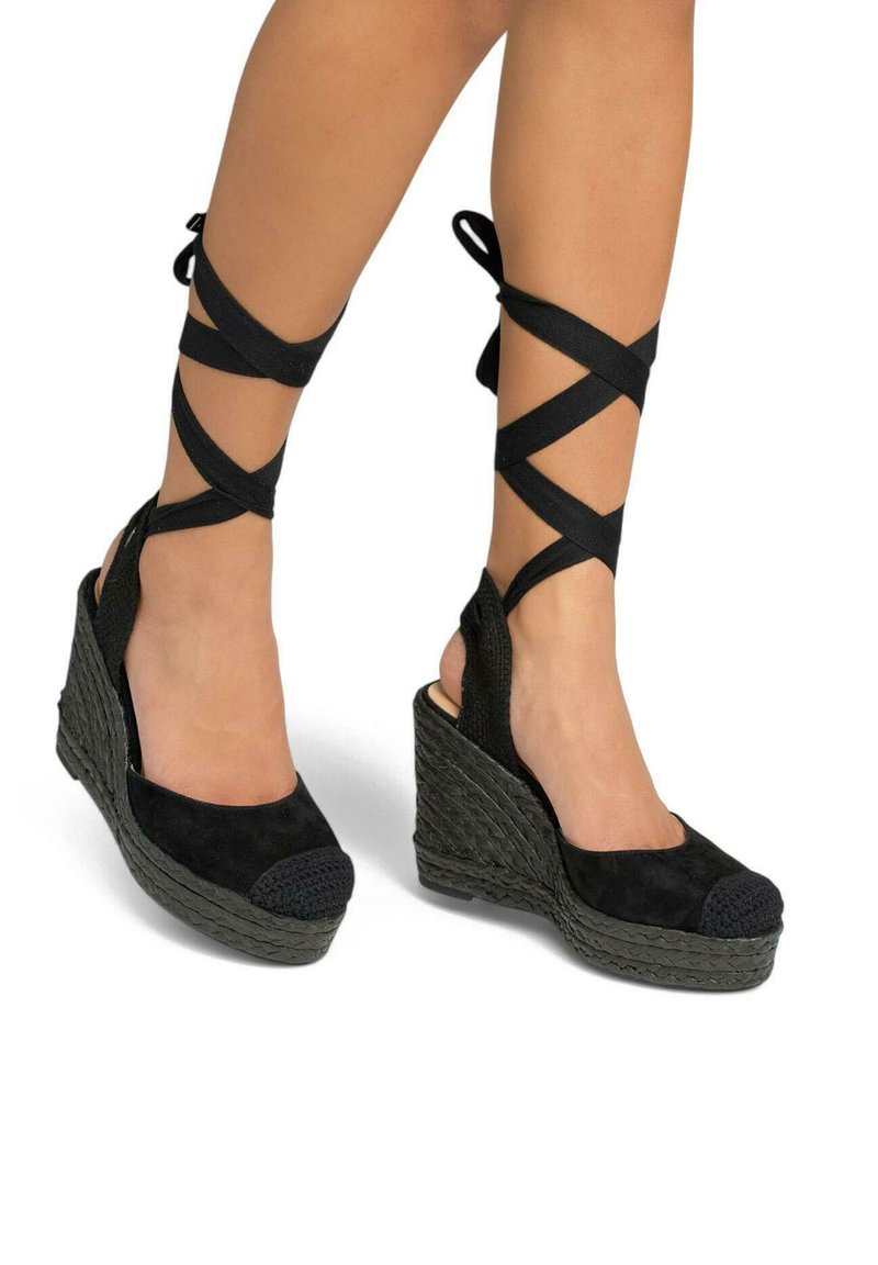 Sandales compensées en suède noir avec une plateforme tissée, comportant des lanières croisées autour de la cheville et un bout texturé.
