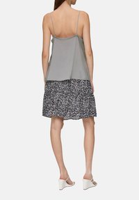 Graues Spaghettiträgershirt mit lockerer Passform, kombiniert mit einem schwarzen Rock mit floralen Muster und Stufen. Das Modell trägt weiße Wedgesandalen.