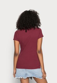 Burgundské tričko s krátkým rukávem a těsným střihem, měkkou texturou a zakřiveným lemem, spárované s denimovou mini sukni s třepenými okraji.