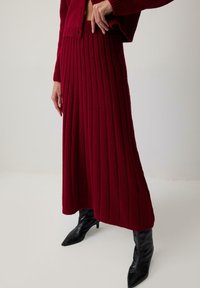 Sukienka dzianinowa w kolorze burgundowym z pionowym prążkowanym wzorem, sięgająca kostek, połączona z czarnymi botkami na szpilce z wysmuklonym noskiem.