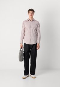 Lys rosa skjorte med knapper, svarte bukser og grå veske. Skjorten har en glatt tekstur; antrekket inkluderer hvite sneakers med beige såler.