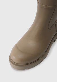 Stivale alla caviglia in gomma marrone con punta arrotondata, superficie testurizzata e suola spessa e scanalata. Presenta un dettaglio decorativo sulla cucitura laterale.