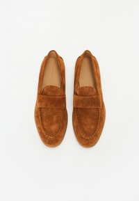 Braune Wildlederslipper mit flachem Design, ausgestattet mit einem breiten Riemen über dem Rist und genähten Details im Zehenbereich.