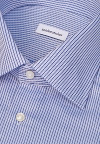 Chemise habillée bleu clair avec de fines rayures diagonales foncées, boutons blancs et une étiquette de marque visible portant la mention "seidensticker" à l'intérieur du col.