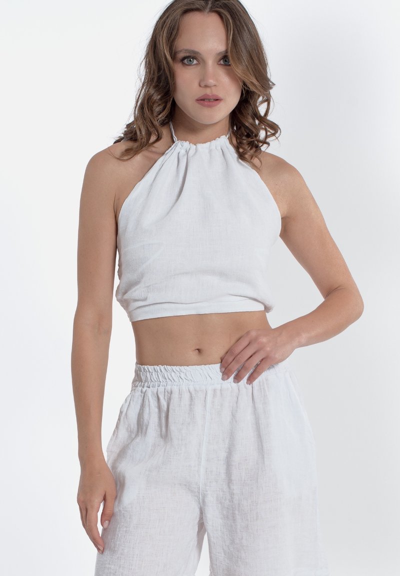 Top corto bianco in lino con scollatura arricciata, abbinato a pantaloni bianchi in lino a vita alta con elastico in vita.