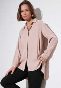 Light pink blouse with a collared neckline, long sleeves, and button front. Made of soft fabric with a loose, flowing silhouette.