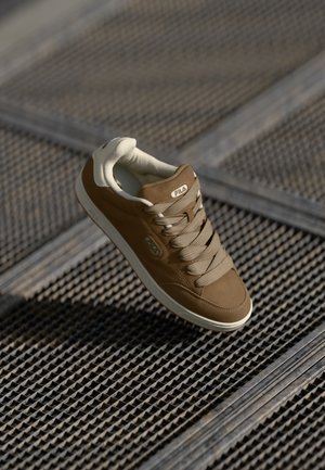 Brown sneaker with a smooth leather upper and beige accents, featuring six laces, a cushioned collar, and a rubber sole. Fila logo visible.