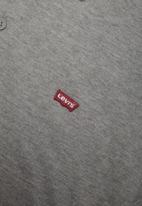 Polo gris en maille à manches courtes, avec un petit logo Levi's rouge et blanc brodé sur le côté gauche près de la poitrine.