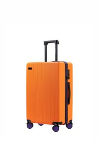 Pomarańczowa walizka z twardą skorupą o pionowej żebrowanej fakturze, czarna wysuwana rączka, fioletowe akcenty zamka błyskawicznego oraz cztery czarne kółka.