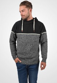 Sweat à capuche avec un haut noir texturé et un bas gris moucheté. Il dispose de cordons de serrage crème et de poignets riblées ainsi qu'un ourlet riblé.