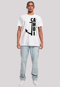 White cotton t-shirt featuring a black graphic design with the word "AHOI" and an anchor. Paired with light blue jeans and white sneakers.
