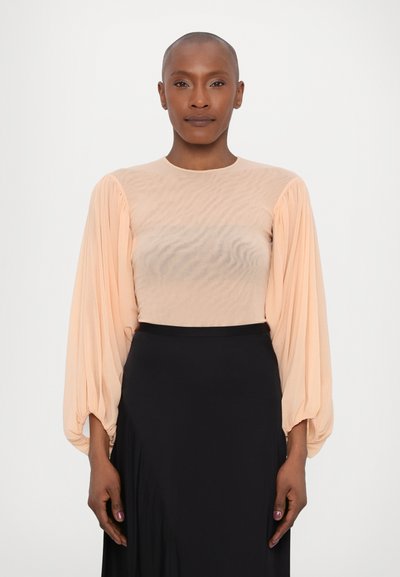 Blouse de couleur pêche avec un tissu transparent et texturé, et de longues manches bouffantes ; associée à une jupe noire unie. Matériau lisse et léger.