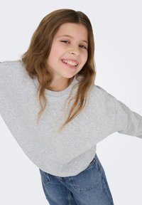 Világosszürke pulóver kerek nyakkivágással és laza szabással, kék farmernadrággal párosítva. Puha tapintású, természetes eséssel, hosszú ujjú.