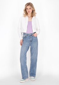 Weißer cropped Hoodie, lilafarbenes Tanktop, hellblaue, hochtaillierte, weite Jeans und mehrfarbige Sneakers. Geschmeidige Texturen und lässiger Stil.