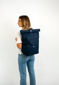 Sac à dos à rouleau bleu marine fabriqué en tissu durable, avec deux zippers latéraux, une poche avant et des bretelles réglables. Texture lisse, design moderne.