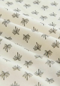 Tissu à fond blanc avec un motif répétitif de petites illustrations minimalistes de palmiers noirs.