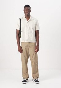 Camisa de lino gris claro de manga corta con bolsillos frontales, combinada con pantalones cargo beige que tienen múltiples bolsillos y zapatillas negras.