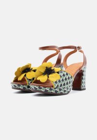 Sandales marron à talons avec plateforme à motifs verts et blancs. Fleurs jaunes avec centres noirs sur les brides. Semelle intérieure marron texturée.