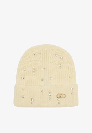 Kremowa czapka beanie ozdobiona klejnotami i perłami, z podwiniętym brzegiem i małą metką z logo po boku.