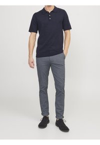 Marinblå pikétröja med platt krage och treknappslå, parat med slim-fit gråa byxor och svarta mockaskor.