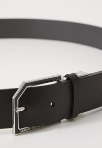 Cintura in pelle nera con una finitura texturizzata, dotata di una fibbia in metallo argentato con un design geometrico e un logo inciso.