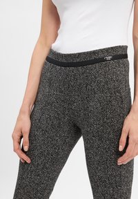 Leggings van een gestructureerde stof met een visgraatpatroon in zwart en grijs, met een zwarte elastische tailleband en logo-detail.