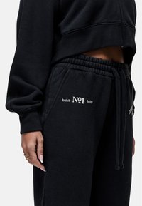 Zwarte cropped sweatshirt en sweatpants gemaakt van textuurstof. Bevat geborduurde tekst "British No1 Design" op de broek en een elastische tailleband.