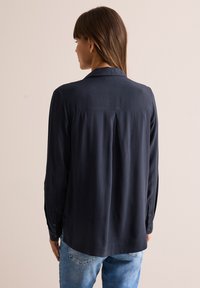 Camicia a maniche lunghe blu navy con una trama morbida, colletto classico e polsini con bottoni; presenta una vestibilità rilassata e un dettaglio con piega sul retro.