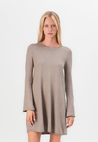 Robe beige à manches longues en tissu doux, avec un col rond et une coupe décontractée, se terminant au milieu de la cuisse et avec des accents cousus sur les bords.