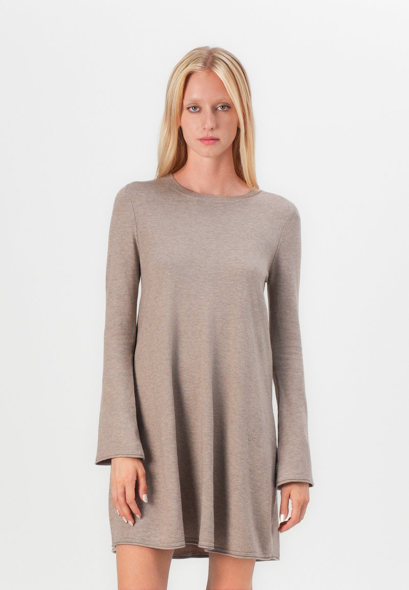 Robe beige à manches longues en tissu doux, avec un col rond et une coupe décontractée, se terminant au milieu de la cuisse et avec des accents cousus sur les bords.