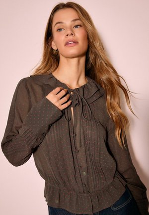 Tummanvihreä pusero, jossa punaista pilkkukuosia, rypytetty pääntie, napitus ja pitkät hihat plisseeratuilla yksityiskohdilla.