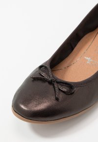 Ballerina in pelle marrone con punta arrotondata, sottile dettaglio a fiocco sul davanti e texture liscia con soletta di un leggero color sabbia.