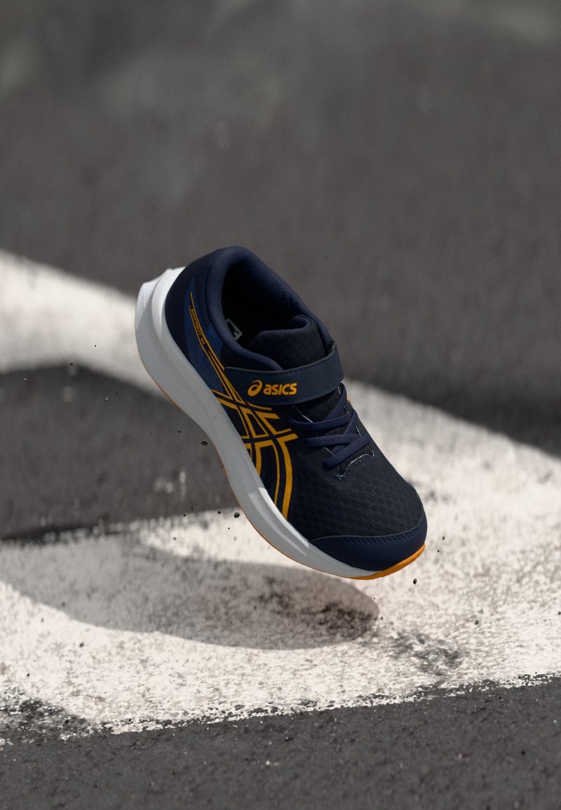 Ναυτικό μπλε αθλητικό παπούτσι με επάνω μέρος από δίχτυ, πορτοκαλί λεπτομέρειες και ιμάντα Velcro. Ελαφρύ σχέδιο με σόλα λευκού και ανοιχτού καφέ χρώματος.