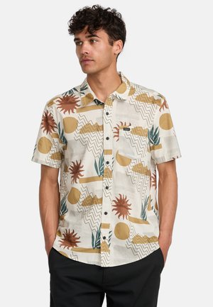 Korte mouwen blouse van lichte stof, met een mix van abstracte patronen, aardetinten en een opgestikte zak op de borst.