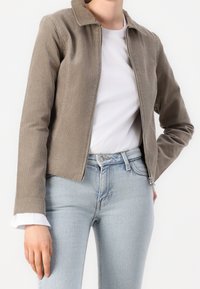 Jasnoszara kurtka ze sztruksu z kołnierzykiem, przednim zamkiem błyskawicznym i dopasowanym krojem. Nosi się ją na białą koszulę, w połączeniu z jasnoniebieskimi jeansami.
