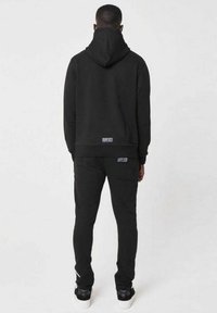 Svart hoodie med dragsko i huvan, tillsammans med matchande svarta byxor i sweatpants-stil. Har minimala varumärkesetiketter på båda plaggen.