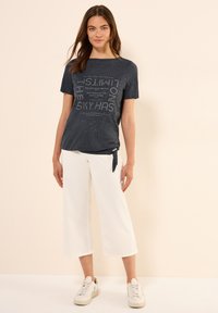 Camiseta azul marina con estampado de texto, de manga corta y corte relajado, combinada con pantalones anchos blancos y zapatillas ligeras.