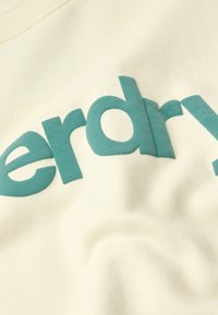 Sudadera de color crema con una textura suave que presenta letras en un vibrante azul aqua que dicen "nerdry" de manera prominente.
