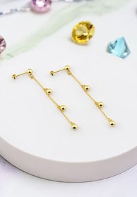 Guldörhängen består av tre sphäriska pärlor kopplade med kedjor, och har en post-stängning. Ytan är glänsande och reflekterande.