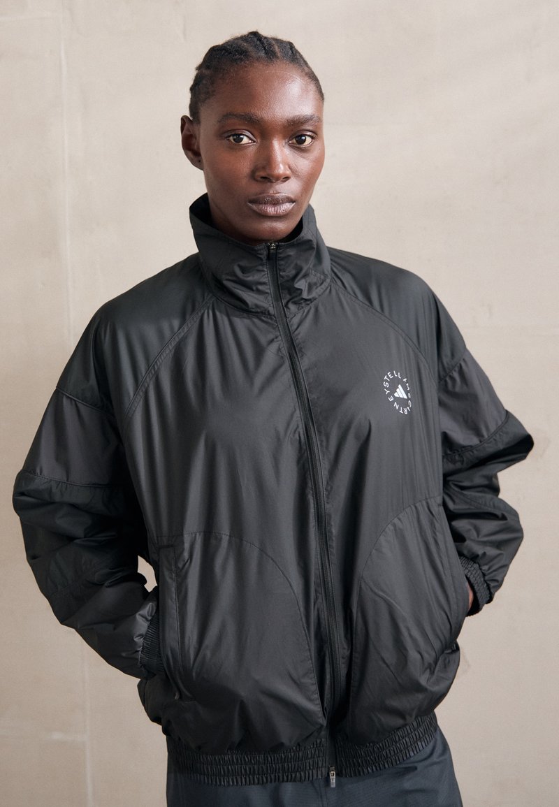 Zwarte nylon windbreaker jacket met een hoge kraag, elastische manchetten en een logo aan de linkerkant. Soepele textuur en een relaxte pasvorm.