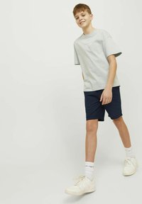 T-shirt en coton gris clair avec un col rond et des manches courtes, associé à un short bleu marine et des baskets blanches, avec une marque discrète sur le t-shirt.