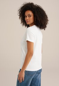 Witte t-shirt met korte mouwen van katoen, met een ronde hals, ontspannen pasvorm en zichtbare stiksels, gecombineerd met blauwe high-waisted jeans.