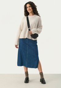 Un pull en tricot crème confortable, une jupe midi en denim avec une fente sur le côté, un sac bandoulière noir et des mocassins sombres. Des chaussettes épaisses aux teintes chaudes.