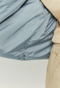 Light blue, nylon outer layer of a jacket, showcasing a smooth texture, elastic drawstring hem with toggle, and a subtle sheen.