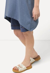 Top asimétrico azul combinado con pantalones cortos azul marino con acentos horizontales, y sandalias blancas con hebillas plateadas y una plataforma de madera.
