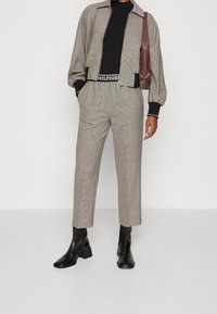 Harmaa ruutukuvioitu lyhyt takki, musta kapea toppi, yhteensopivat ruutukuviolliset housut, mustat lohkokorolliset nilkkurit, kädessä bordeauxinpunainen laukku, tyylikäs muotoilu.