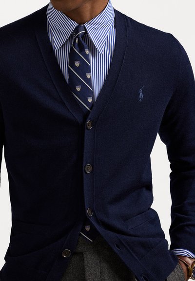 Navy wool cardigan with a V-neck, three buttons, and a small logo. Worn over a blue and white striped shirt and patterned tie.