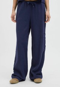 Navy wijde broek gemaakt van zachte stof met een tailleband met trekkoord en zijzak. Zichtbare stiksels voegen detail toe aan het ontspannen ontwerp.