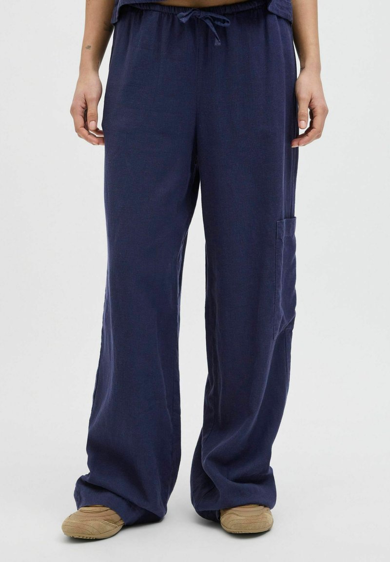 Navy wijde broek gemaakt van zachte stof met een tailleband met trekkoord en zijzak. Zichtbare stiksels voegen detail toe aan het ontspannen ontwerp.