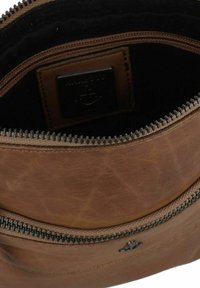 Borsa in pelle marrone con una texture morbida, chiusura con cerniera e interno nero. Presenta un'etichetta con il marchio e dettagli in hardware argentato.